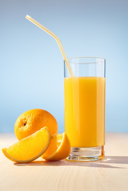 Sinaasappel, glas met jus d'orange en stro op houten tafel.