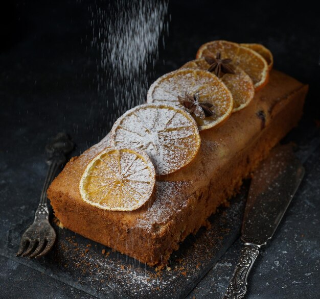 Sinaasappelcake, gedecoreerd met gekarameliseerde sinaasappels en cacao en poedersuiker op een donkere stenen ondergrond