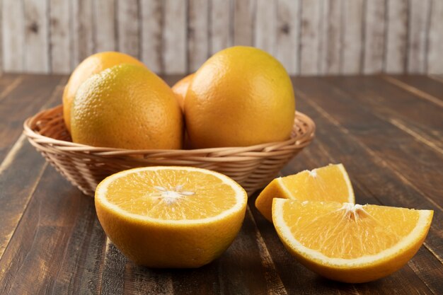 Sinaasappelen in een mand met gesneden fruit over houten lijst.