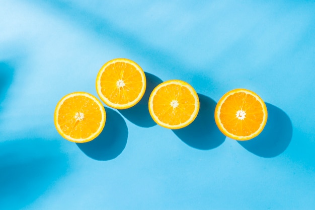 Sinaasappelen op een blauw oppervlak onder natuurlijk licht met schaduwen. Hard licht. Concept van voeding, gezond eten, rust in de tropen, vakantie en reizen, vitaminen. Plat lag, bovenaanzicht.