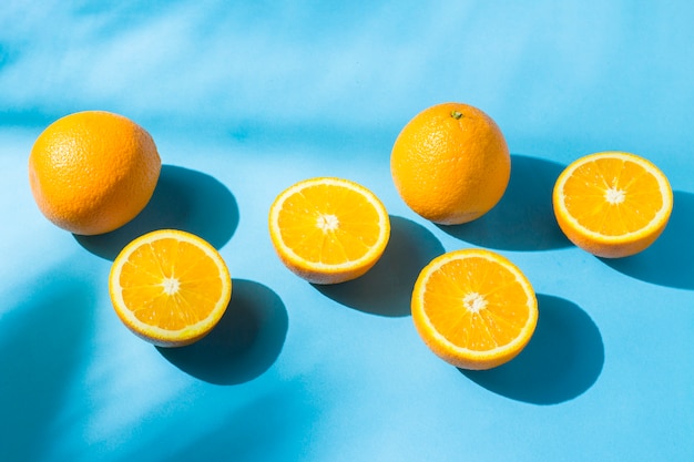 Sinaasappelen op een blauw oppervlak onder natuurlijk licht met schaduwen. Hard licht. Concept van voeding, gezond eten, rust in de tropen, vakantie en reizen, vitaminen.