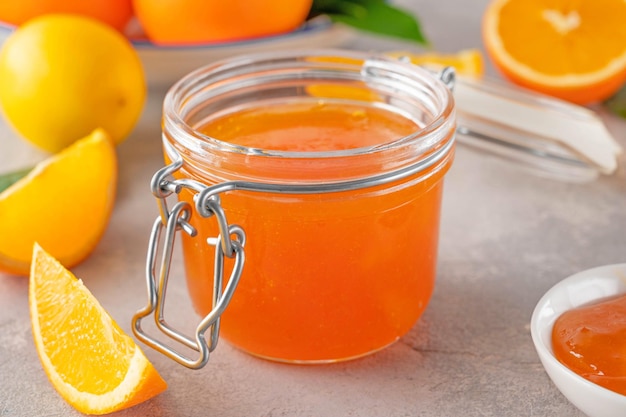 Sinaasappelmarmelade of sinaasappeljam in glazen pot met vers fruit op een grijze achtergrond