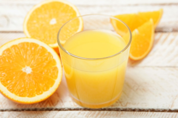 Sinaasappelsap in een glas sinaasappels en stukjes sinaasappel op tafel