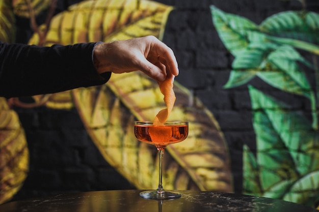 Sinaasappelschil garnering in een cocktailglas zetten met een drankje