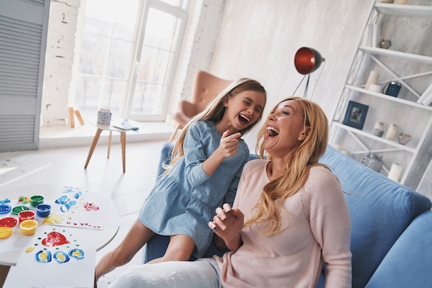 Sincere joy. Top view of mother and daughter laughing while painting at home