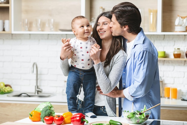 Sincere love. Young family embracing with baby at kitchen, empty space