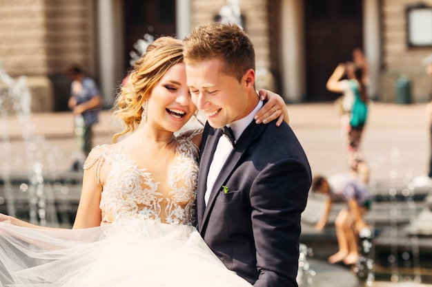 Sincere smiles of beautiful newlyweds on the background of a fountain and old city