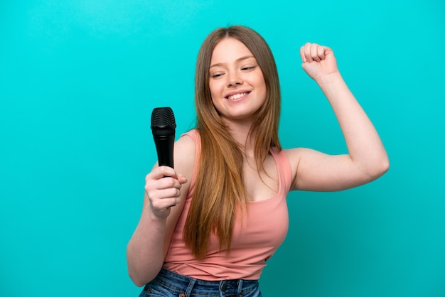 Singer caucasian woman picking up a microphone isolated on blue background celebrating a victory