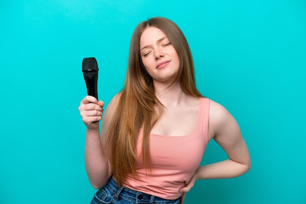 Singer caucasian woman picking up a microphone isolated on blue background suffering from backache for having made an effort