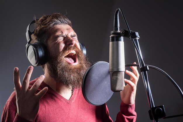 Singer man wearing headphones is performing a song with a microphone while recording in a music stud