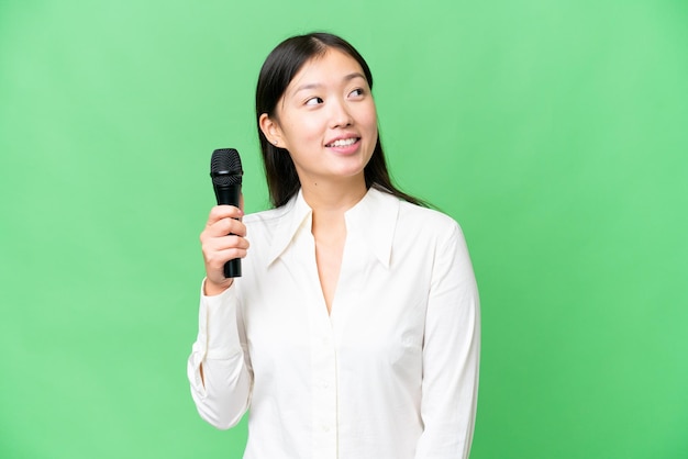 Singer picking up a microphone over isolated chroma key background looking up while smiling