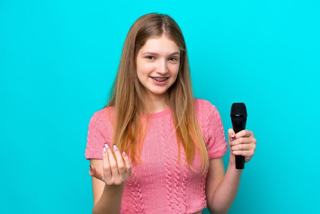 가수 러시아 소녀가 파란색 배경에 격리된 마이크를 들고 손을 잡고 초대합니다.