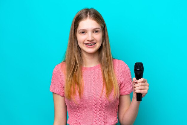 Singer Russian girl picking up a microphone isolated on blue background smiling a lot