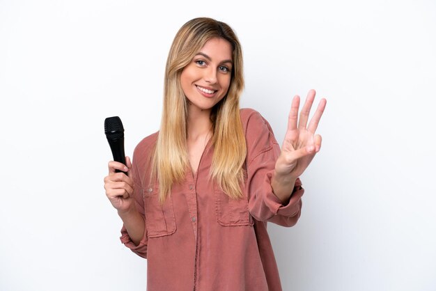 Singer Uruguayan woman picking up a microphone isolated on white background happy and counting three with fingers