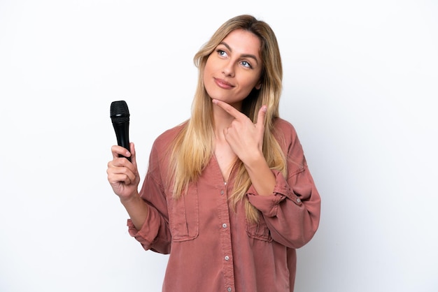 Singer Uruguayan woman picking up a microphone isolated on white background looking up while smiling