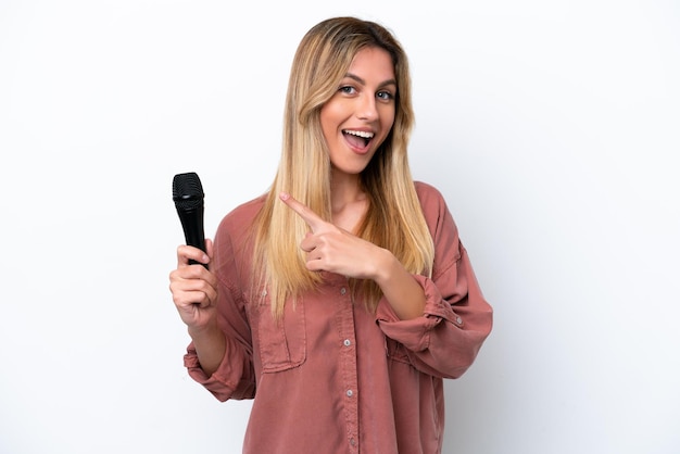 Singer Uruguayan woman picking up a microphone isolated on white background pointing to the side to present a product