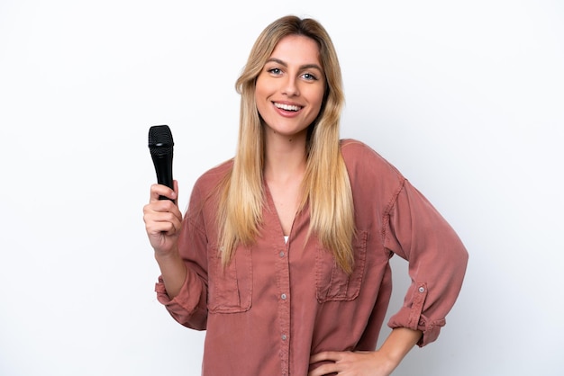 Singer Uruguayan woman picking up a microphone isolated on white background posing with arms at hip and smiling