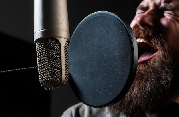 singer with expressive face closeup wearing headphones is performing a song with a microphone while recording in a music studio