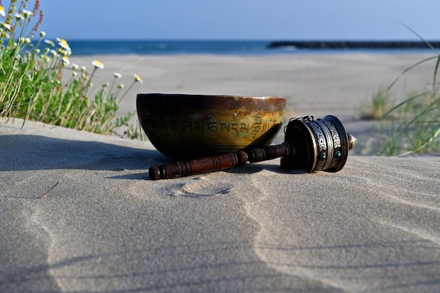 Singing bowl on the beach and prayer wheel. Mantra translation. transform your impure body