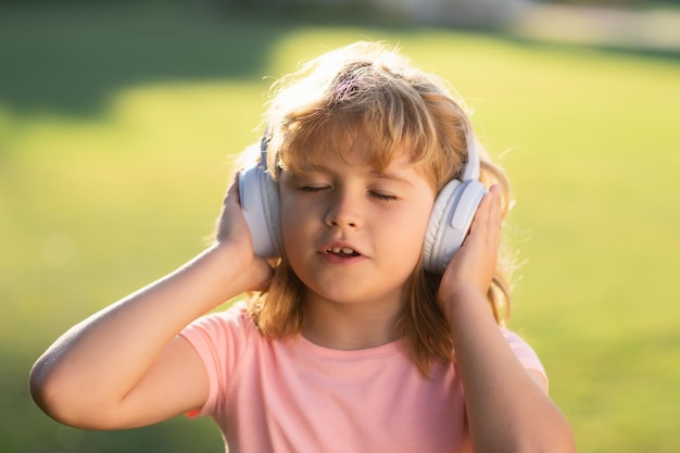 Singing children daydreaming child enjoys listens to music in headphones over green grass background