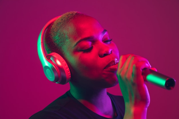 Singing in headphones. African-american young woman's portrait on purple background. Beautiful model in black shirt. Concept of emotions, facial expression, sales, ad, inclusion, diversity. Copyspace.