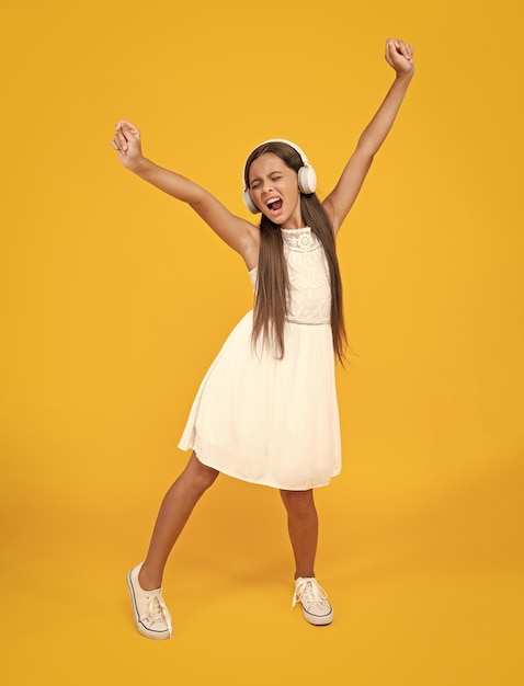 singing teen girl listen music in headphones and dancing on yellow background