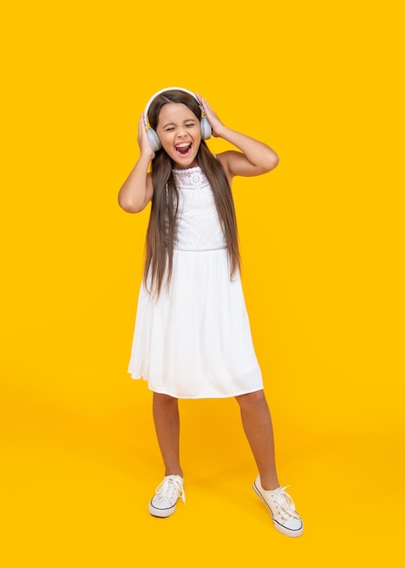 Singing teen girl listen music in headphones on yellow background