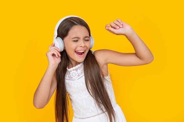 Singing teen kid listen music in headphones on yellow background