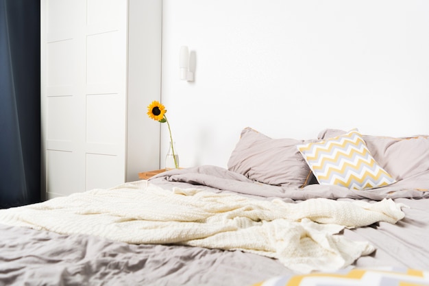 Single beautiful yellow sunflower in vase near bed in bedroom