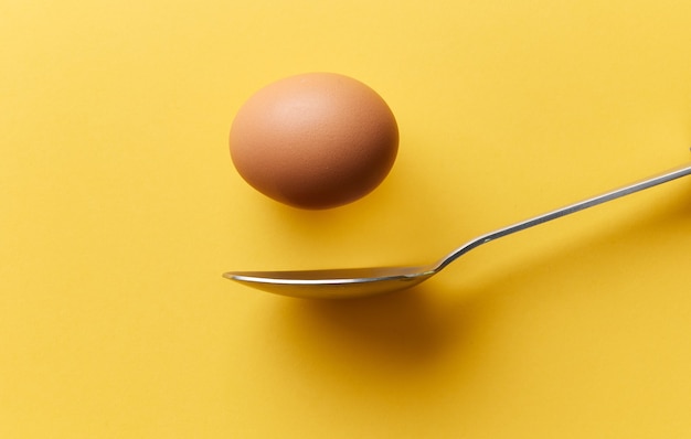 Photo single brown chicken egg falling into spoon on yellow background