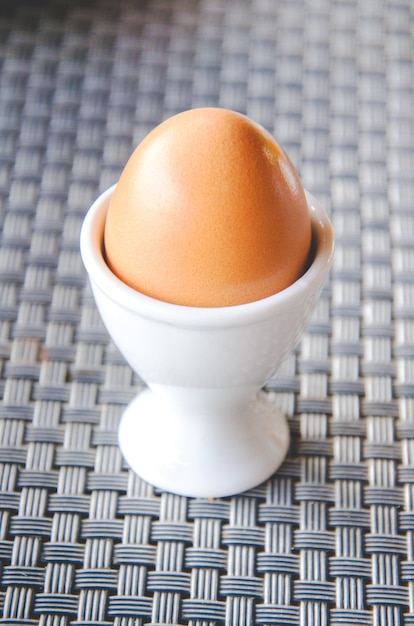 A single brown egg in a white eggcup on the napery.