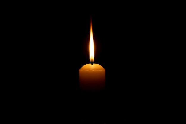 Одно горящее пламя свечи или свет, горящий на большой белой свече на черном или темном фоне на столе в церкви на рождественские похороны или поминальную службу с копией пространства