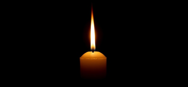 Photo single burning candle flame or light is glowing on a big yellow candle on black or dark background on table in church for christmas funeral or memorial service with copy space