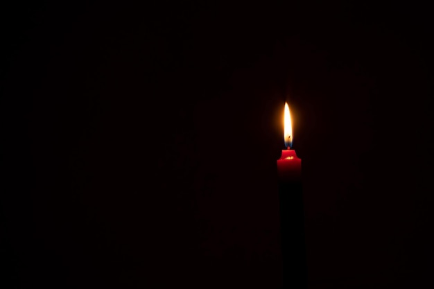Foto una singola fiamma o luce di una candela in fiamme sta brillando su una candela arancione su sfondo nero o scuro sul tavolo in chiesa per il funerale di natale o il servizio commemorativo con spazio di copia