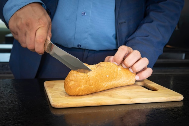 Un solo uomo d'affari si prepara un panino in cucina. le mani dell'uomo che tagliano il pane sulla tavola di legno.