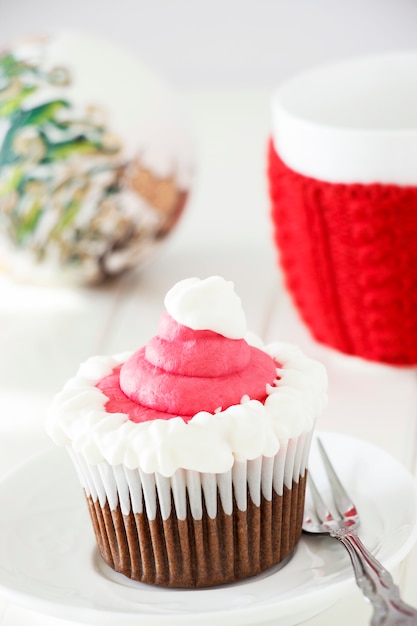 Single Christmas homemade chocolate cupcake with frosting white pink buttercream. White wooden background.