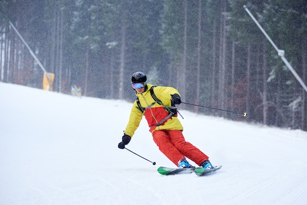 Single descent of young male skier downhill skiing and doing carve turn on high wooded slope. Skiing during snowfall