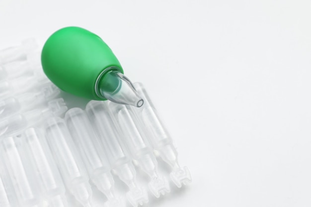 Single dose ampoules of sterile isotonic sea water solution and nasal aspirator on white background closeup Space for text