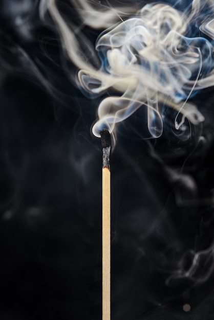 Photo a single extinguished match with smoke rising up isolated on a black background