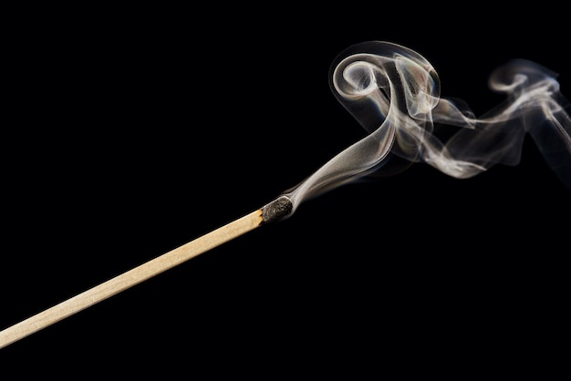 Photo a single extinguished match with smoke rising up isolated on a black background