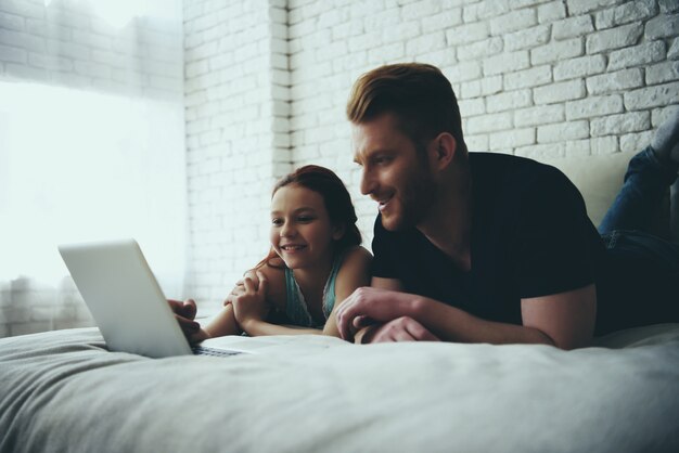 Single father and daughter lie on bed and look.