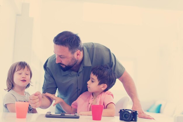 single father at home with two kids playing games and giving education lessons on tablet  computer at modern home