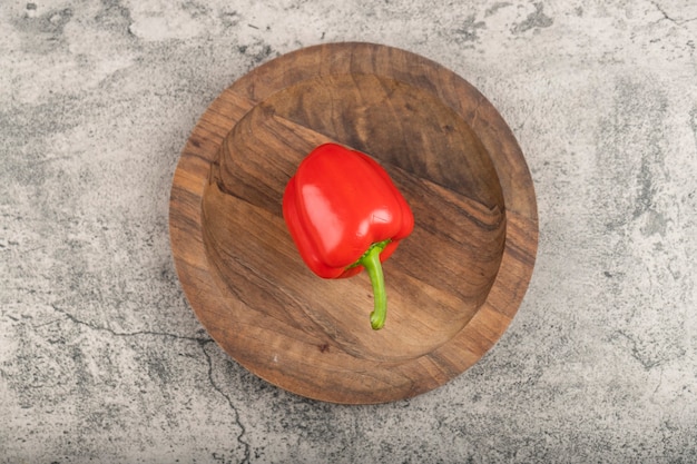 Single fresh red bell pepper on wooden plate