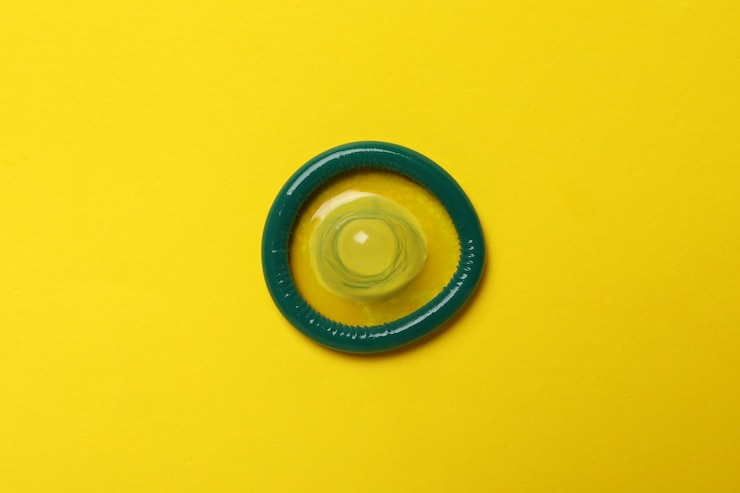 Photo single mint condom on yellow wall, top view