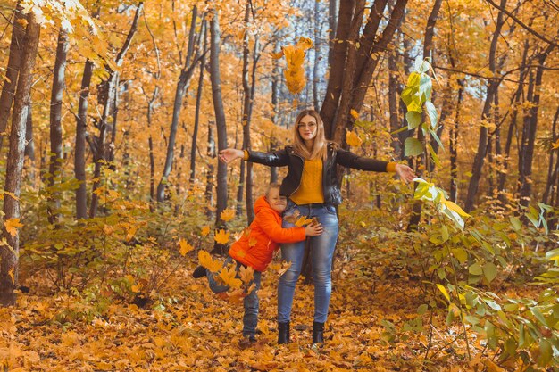 Single parent family playing with autumn leaves in park. Happy mom and son throw autumn leaves up in fall park.