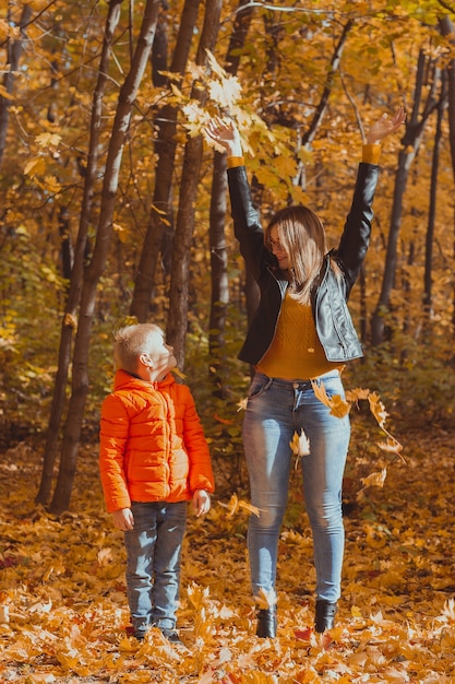 Single parent family playing with autumn leaves in park happy mom and son throw autumn leaves up in