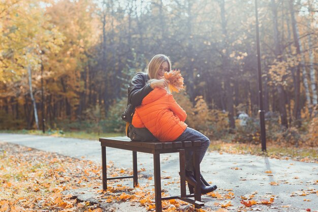 Single parent mother and child boy in the autumn in park sit on bench fall season and family concept