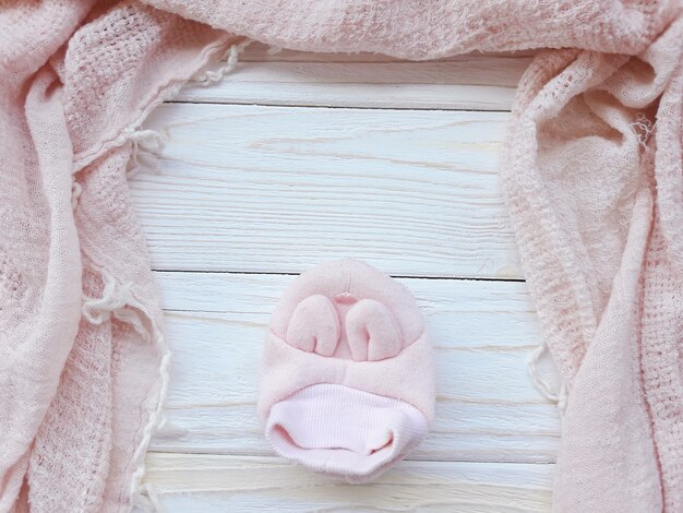 Single pink baby shoe and a pink scarf on a white wooden 