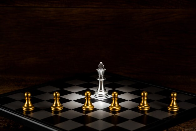 single silver king chess surrounded by a number of gold chess pawn pieces 