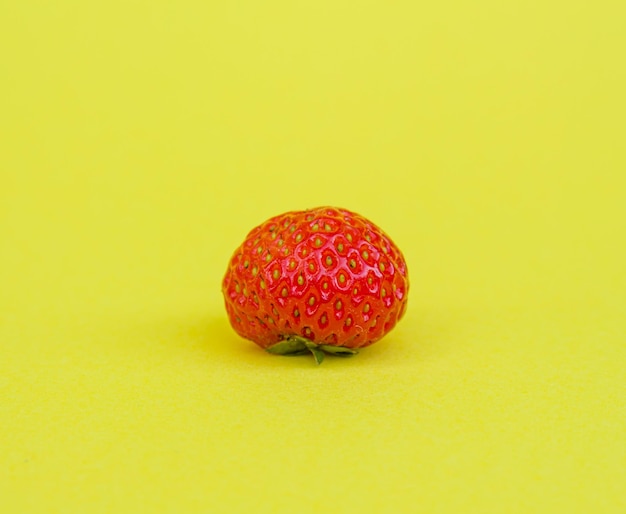 Single strawberry isolated on yellow background.